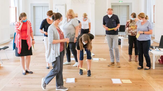 Aktive Workshopteilnehmer im Resilienz-Training sortieren Arbeitsblätter auf Holzfußboden