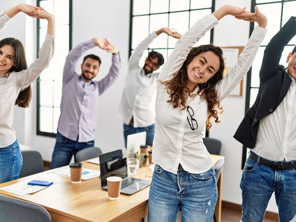 eine Gruppe junger Menschen im Büro die sich im Stehen strecken
