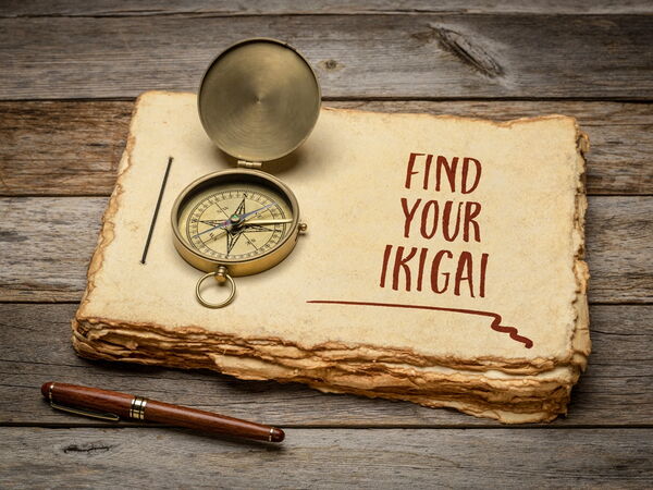 KI-Grafik: ein Stapel vergilbte Blätter auf denen ein Kompass liegt und "find your IKIGAI" stehe und einem alten Füller der davor auf dem Holztisch liegt